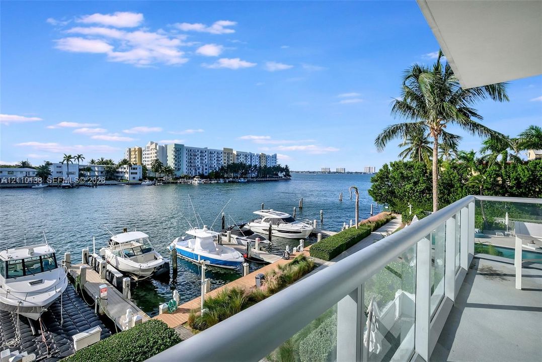 Covered balcony featuring glass railing, overlooking a waterway with private boat slips and mature palm trees