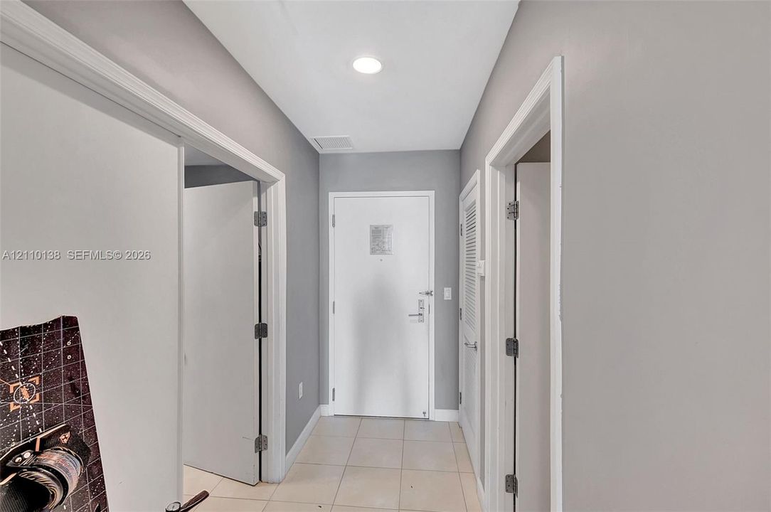 Hallway featuring neutral-toned walls, recessed lighting, tile flooring, and white interior doors with satin nickel hardware