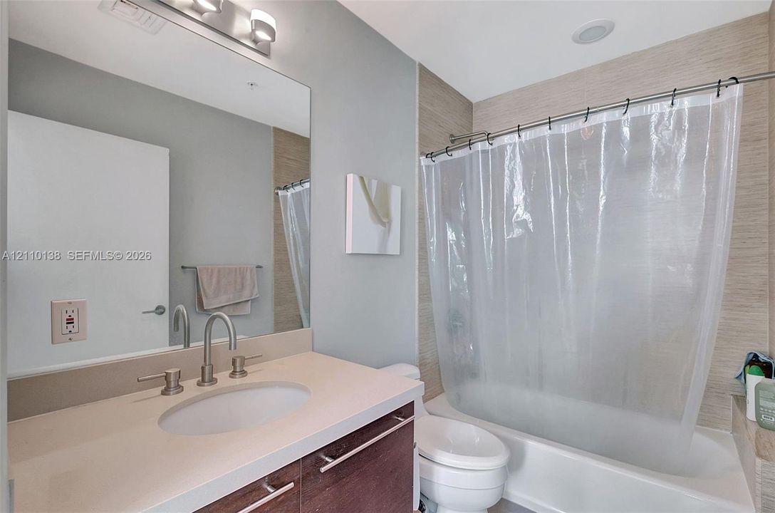 Bathroom featuring a wood-tone vanity cabinet, solid-surface countertop with an integrated basin, brushed-metal widespread faucet, and a large wall-mounted mirror with integrated lighting