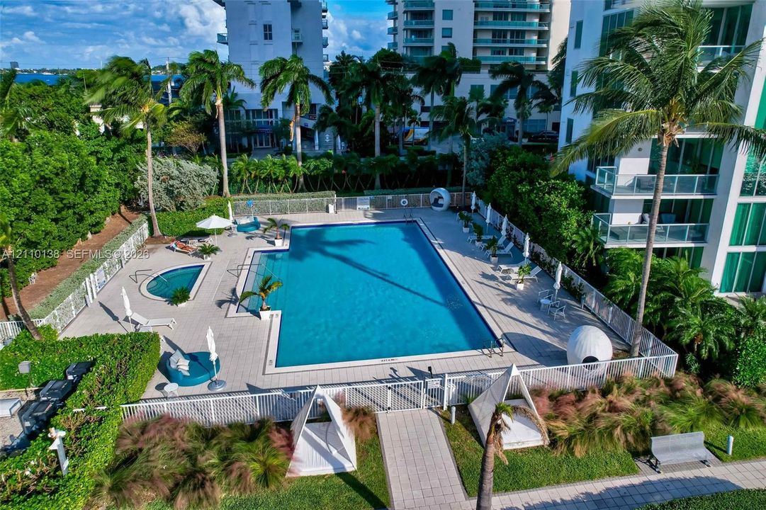 Swimming pool and separate hot tub with tiled decking, enclosed by perimeter fencing and surrounded by landscaping