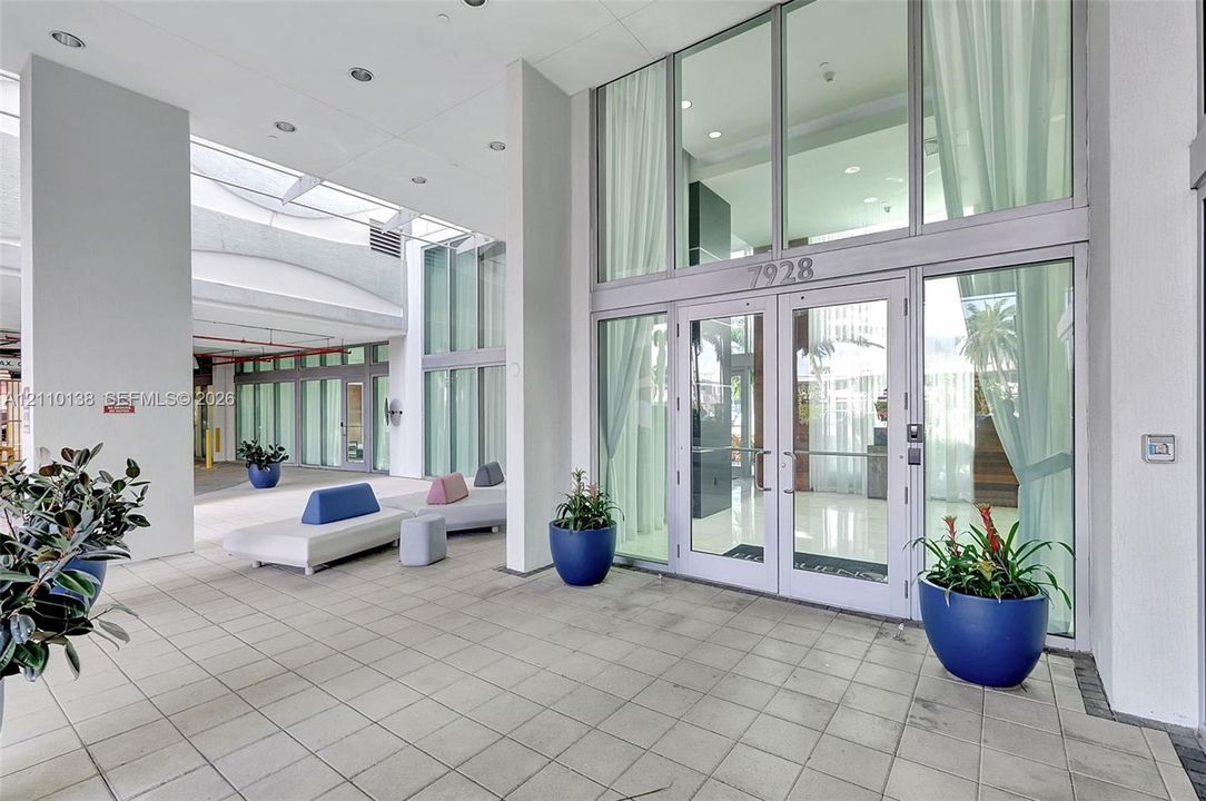 Covered entryway featuring expansive floor-to-ceiling glass paneling, double-door entrance, recessed ceiling lighting, and large-format tile flooring