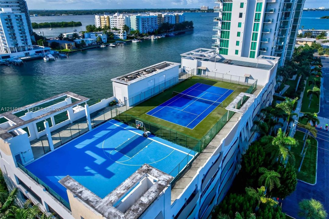 Rooftop recreation area featuring a hard-court tennis surface, basketball court, and perimeter security fencing