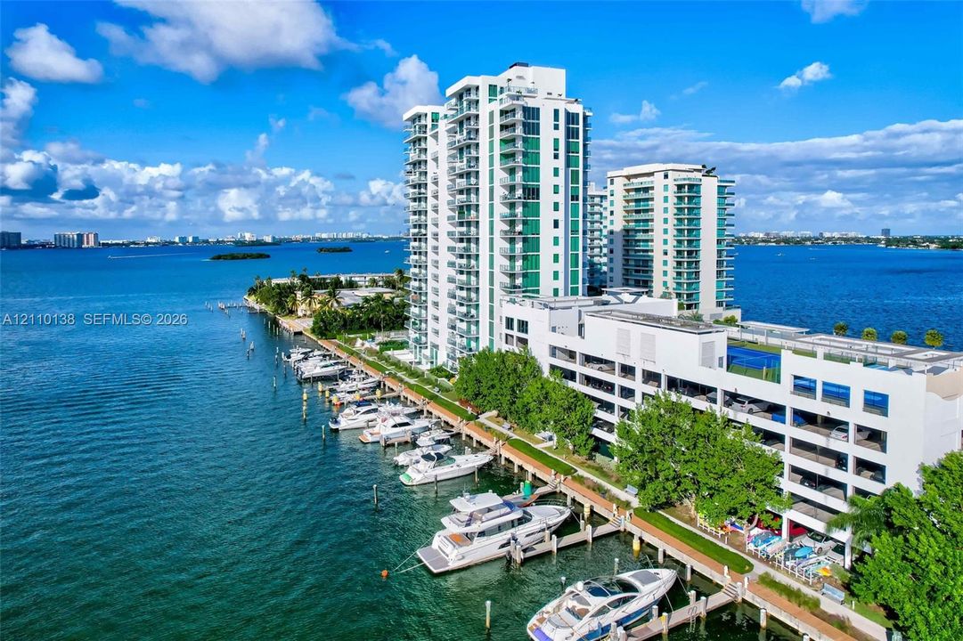 High-rise waterfront complex featuring private deep-water boat slips, expansive balcony tiers, an elevated outdoor pool, and tennis courts situated along the shoreline
