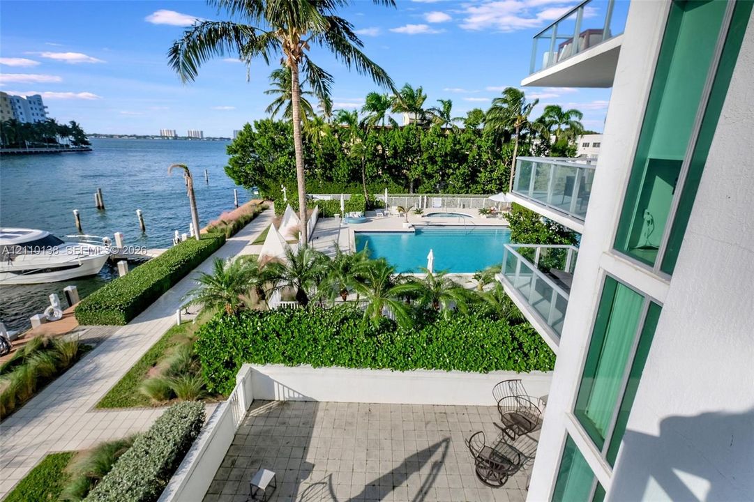 Waterfront balcony featuring glass railings, overlooking a swimming pool, paved patio, and private boat dock