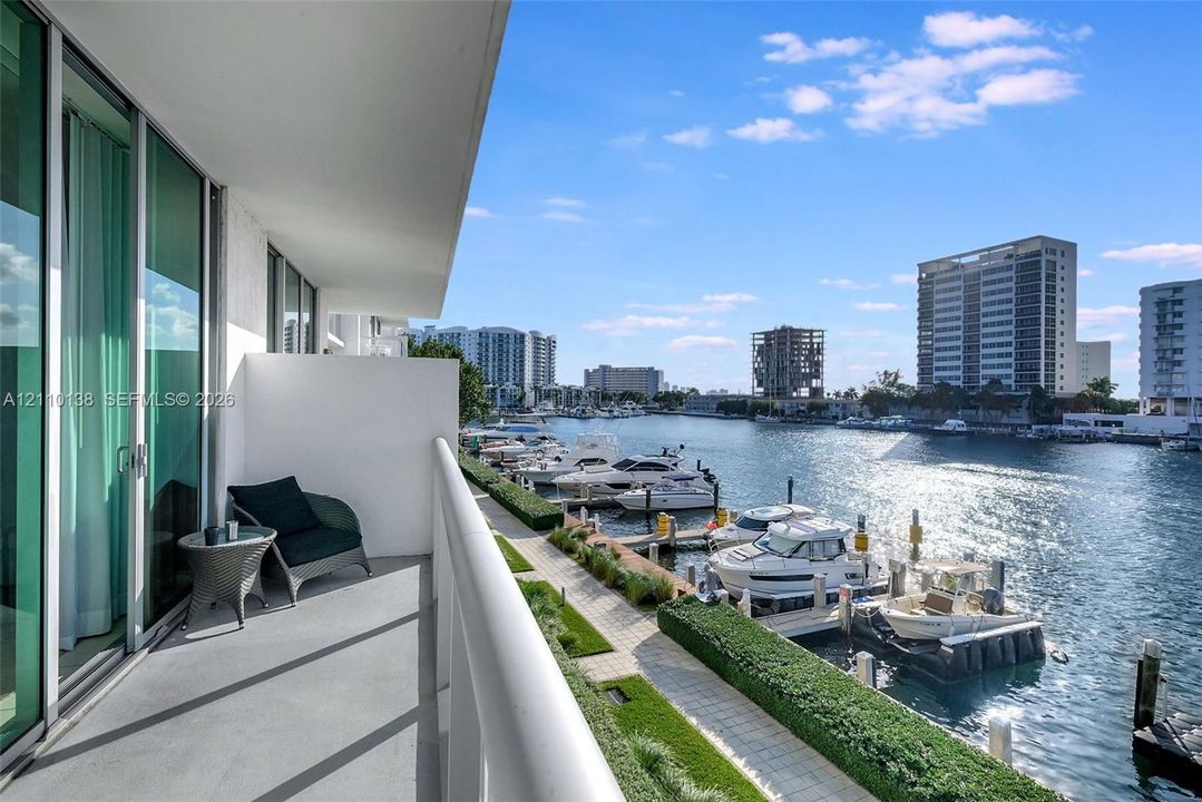Covered balcony featuring glass sliding doors, concrete flooring, and metal railing overlooking a private marina with deep-water slips