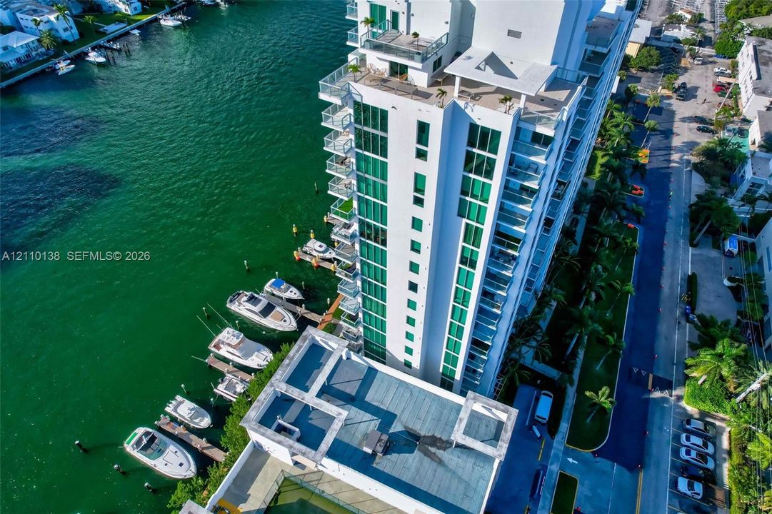 High-rise waterfront building featuring private boat slips, extensive glass window panels, multiple balconies with glass railings, and ground-level parking