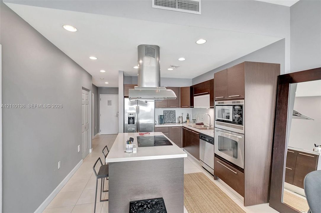 Kitchen featuring flat-panel cabinetry, a central island with a quartz countertop, stainless steel appliances, a chimney-style range hood, and tile flooring