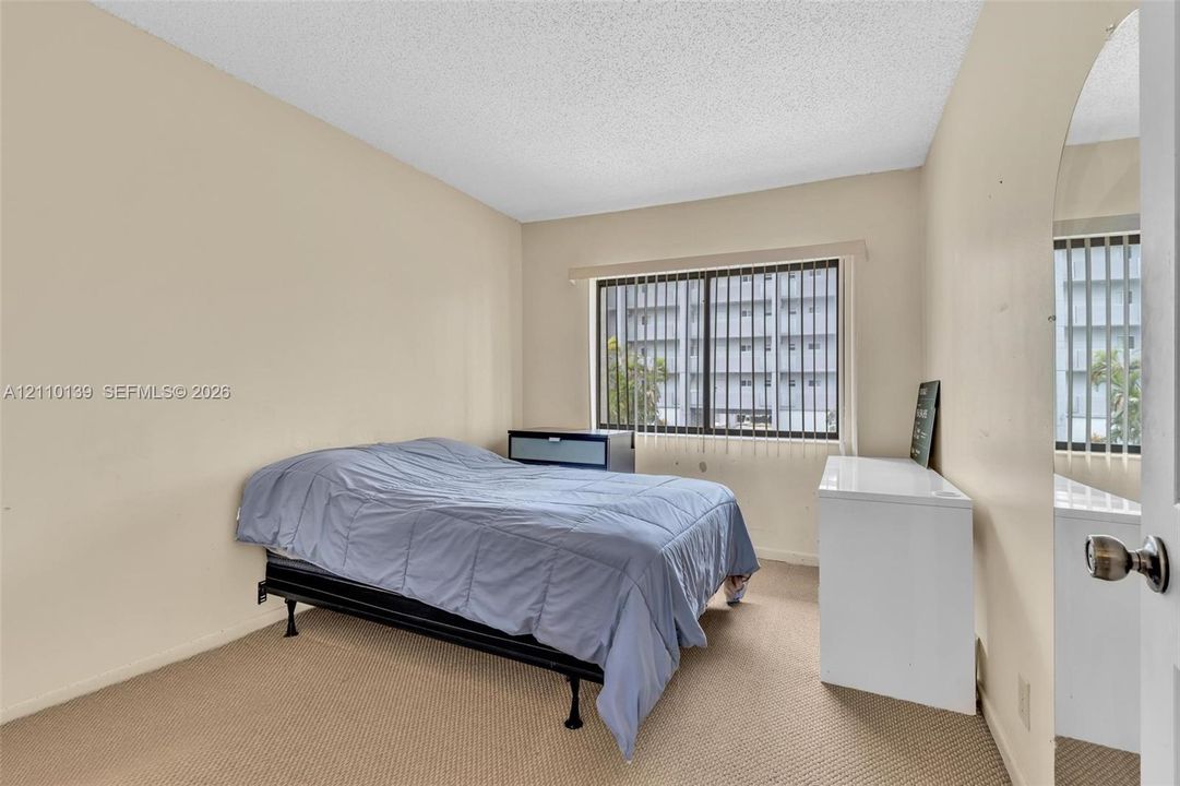 Neutral-toned interior space featuring carpeting, a multi-pane sliding window with vertical blinds, and a mirrored door