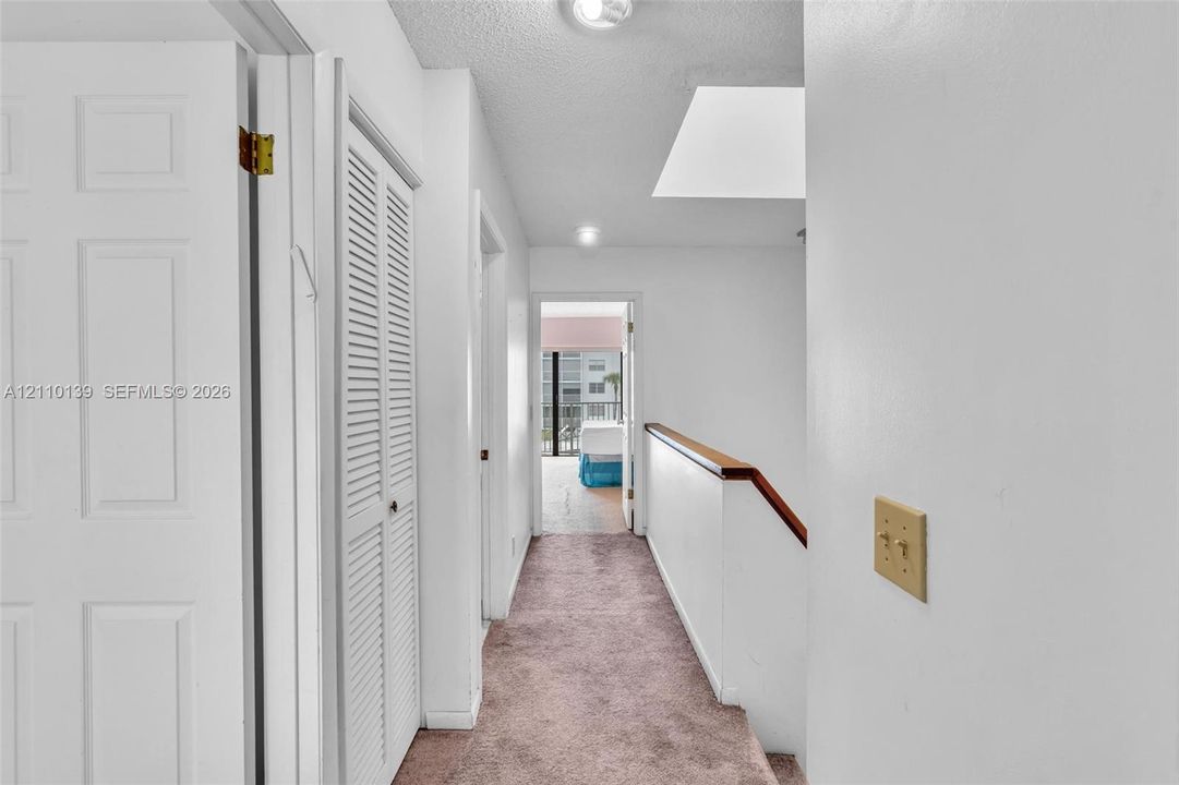 Interior hallway featuring carpeted flooring, a skylight, multi-panel doors, louvered-style closet doors, and a staircase with a wooden handrail