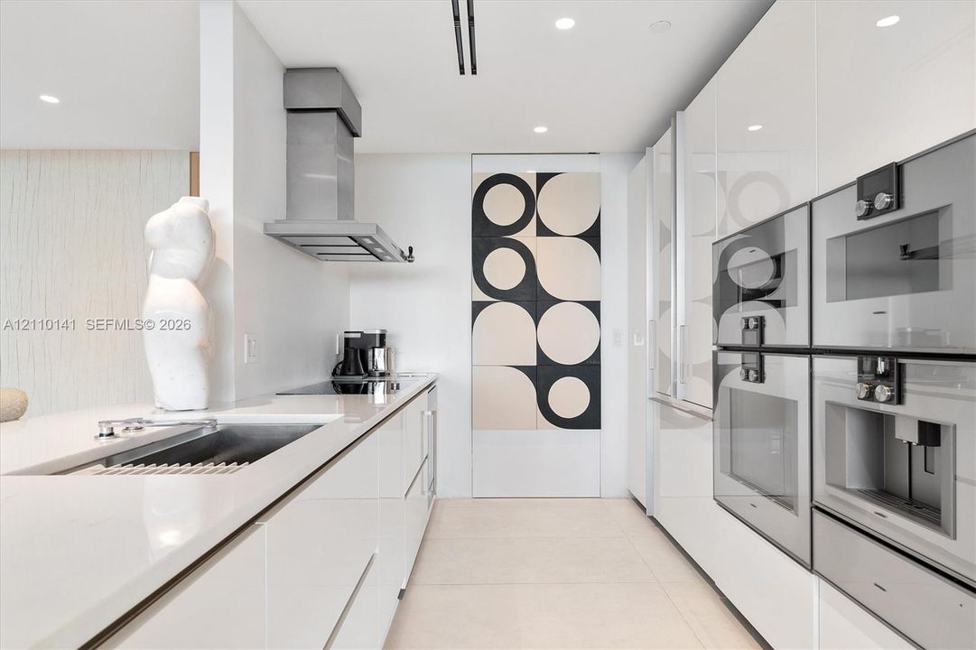 High-gloss cabinetry, integrated stainless steel appliances, recessed ceiling lighting, stone-finish countertops, and a seamless sink basin