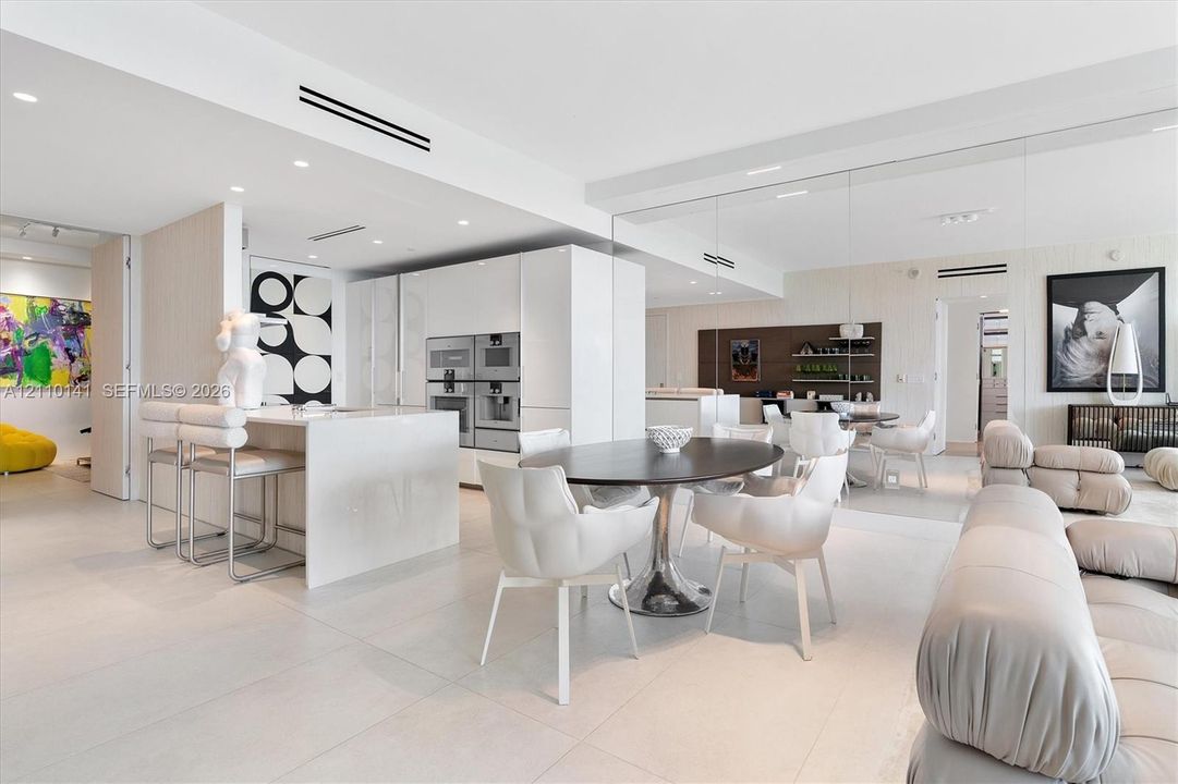 Contemporary interior featuring large-format tile flooring, high-gloss flat-panel cabinetry, a waterfall-edge kitchen island, integrated stainless steel appliances, and mirrored wall panels