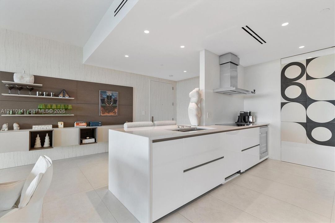 Modern kitchen featuring a central island with countertop, sleek handle-less cabinetry, stainless steel range hood, recessed ceiling lighting, and tile flooring