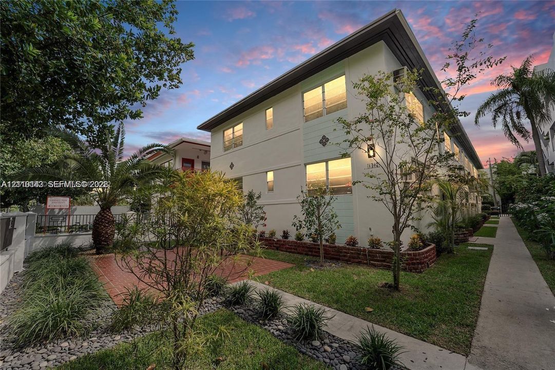 Multi-story exterior featuring light-toned stucco facade, paved brick patio, and manicured landscaping with stone border accents