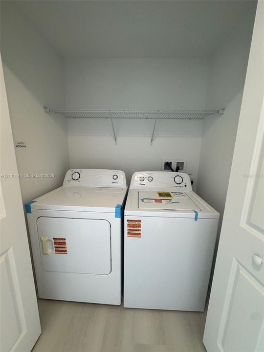 Laundry closet featuring side-by-side white washer and dryer units, a white wire shelf, and light-toned flooring