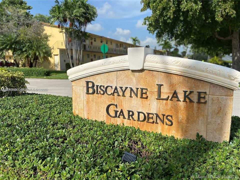 Stone-clad community monument sign featuring dimensional metal lettering and manicured landscape hedging