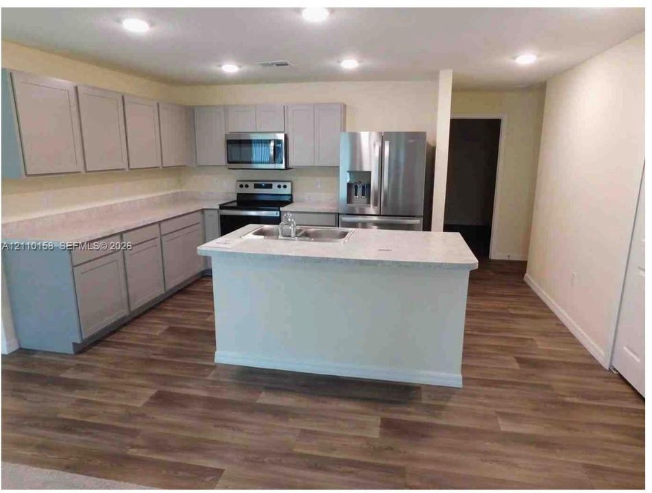 Kitchen featuring light-toned cabinetry, stone-finish countertops, stainless steel appliances, a center island with a dual-basin sink, and wood-finish flooring