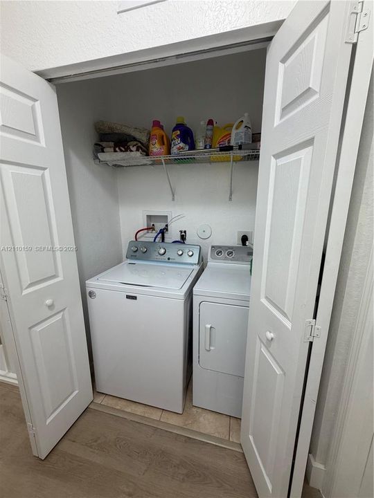 Laundry closet featuring white bi-fold doors, white top-load washer and dryer, and wire shelving