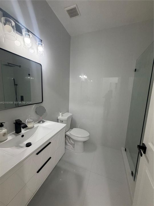 Bathroom featuring a white geometric-pattern vanity, rectangular vessel sink, matte black faucet, wall-mounted rectangular mirror, and glass-enclosed shower