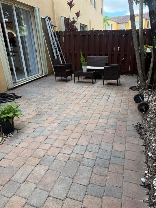 Private rear patio featuring concrete paver flooring, full-height privacy wood fencing, and sliding glass door access
