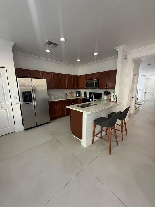 Kitchen featuring dark-toned cabinetry, light-colored countertops, stainless steel appliances, a peninsula with an undermount sink, and recessed lighting