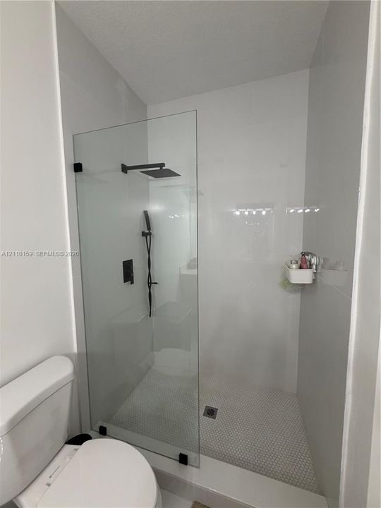 Walk-in shower featuring a frameless glass partition, matte black rainfall showerhead, handheld sprayer, and hexagon tile floor