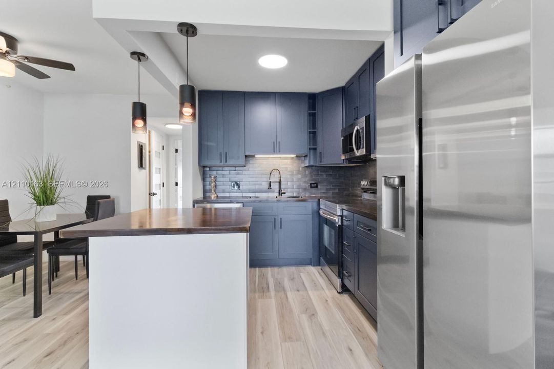 Kitchen featuring dark blue cabinetry, wood-finish island countertop, stainless steel appliances, subway tile backsplash, and cylindrical pendant lighting