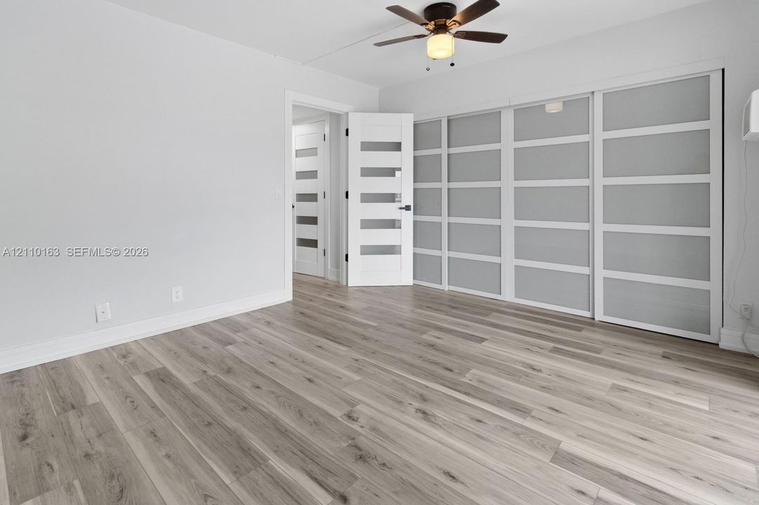 Wood-finish flooring, multi-panel sliding closet doors with frosted glass inserts, five-panel interior doors, and a ceiling fan with integrated lighting