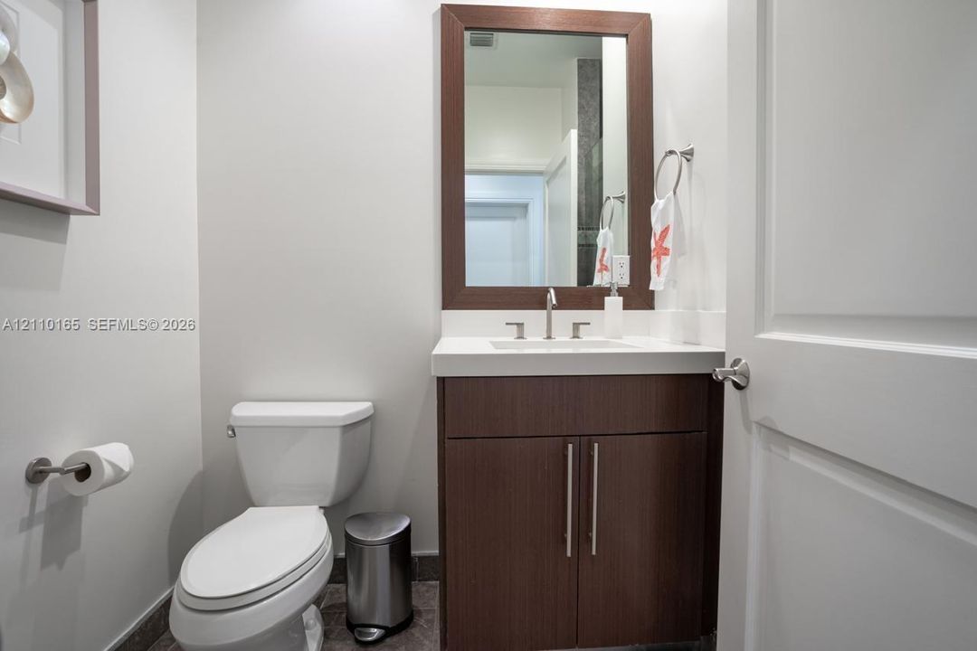 Bathroom featuring a dark wood-finish vanity with a rectangular sink, white countertop, brushed-metal hardware, and a matching framed wall mirror