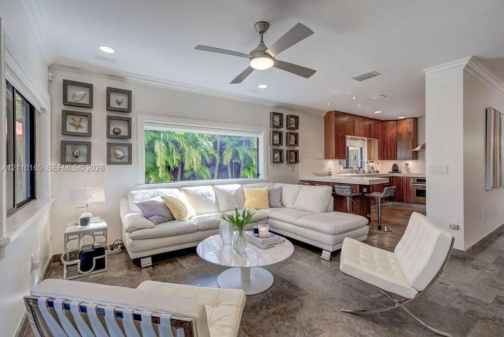 Open-concept interior featuring oversized tile flooring, a horizontal picture window, recessed lighting, and a kitchen with wood-finish cabinetry and a breakfast bar
