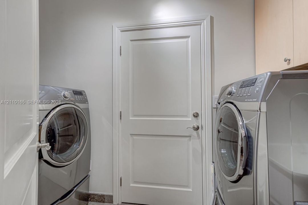 Laundry space featuring light-toned upper cabinetry, solid-core panel door with satin nickel hardware, and tile flooring