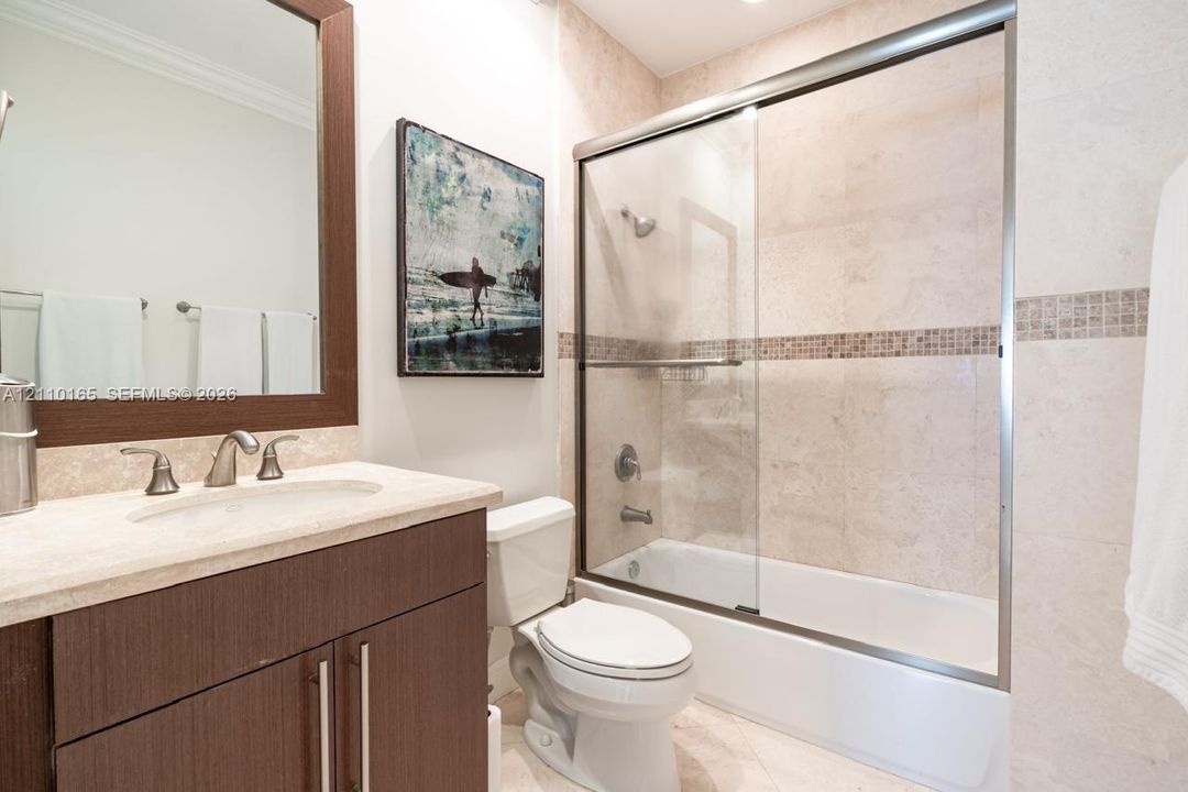 Bathroom featuring a dark wood-finish vanity with a stone countertop, an integrated sink with polished metal fixtures, a framed mirror, and a tub-shower combination enclosed by glass sliding doors with tiled surrounds