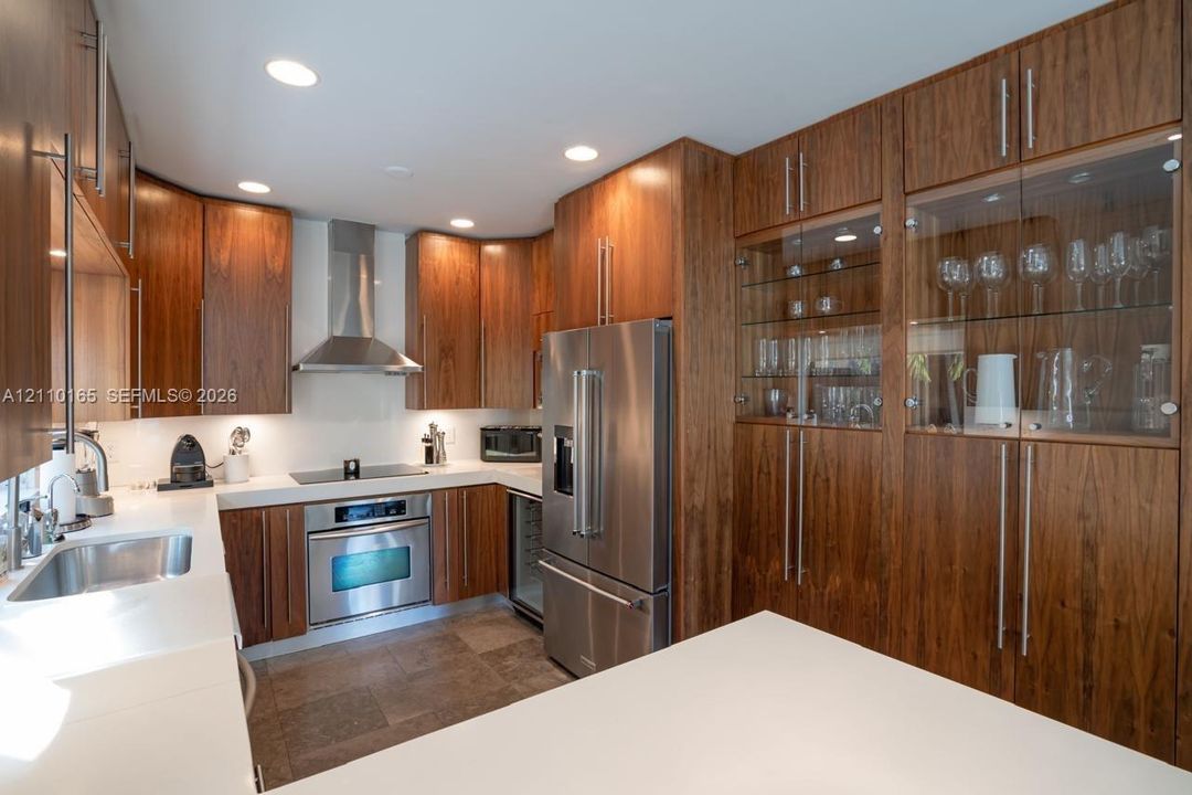Kitchen featuring wood-finish cabinetry, white countertops, stainless steel appliances, glass-front upper cabinets, and a stainless steel undermount sink