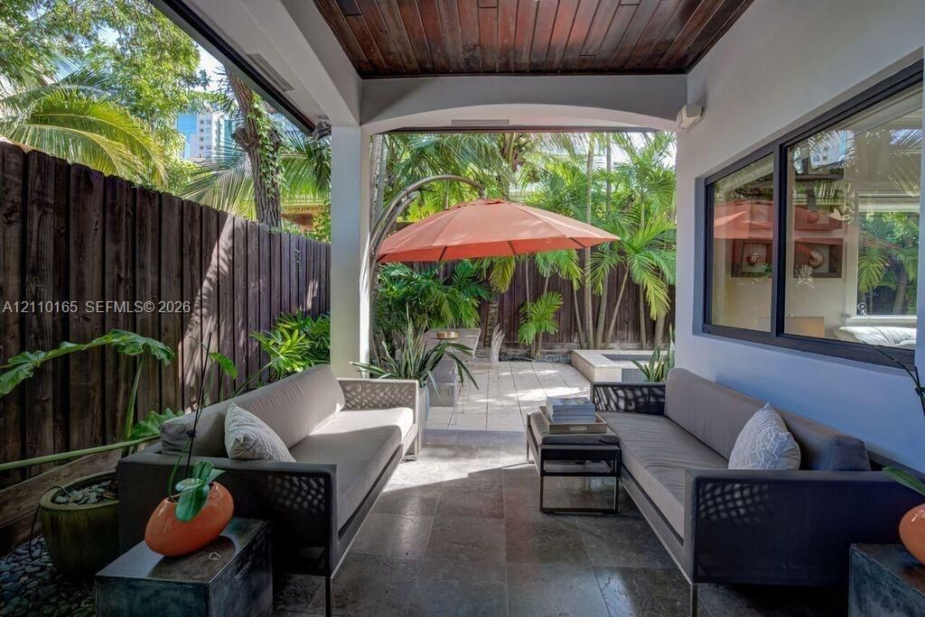 Covered patio featuring a stained wood plank ceiling, stone flooring, arched structural detailing, and a high privacy fence
