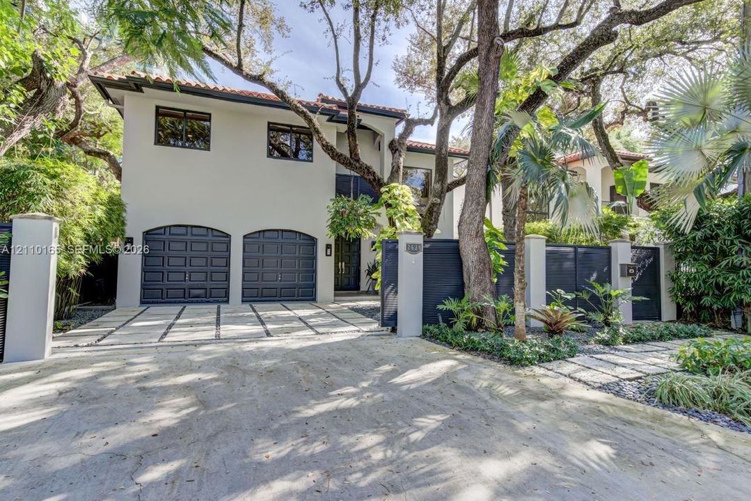 Two-story residence featuring a tile roof, dual arched garage doors, concrete paver driveway with integrated stone edging, and private gated entry