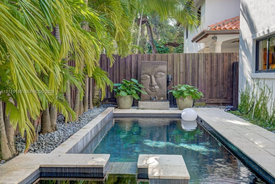 Outdoor pool with stone coping, decorative water feature, privacy fencing, and stone-finish decking