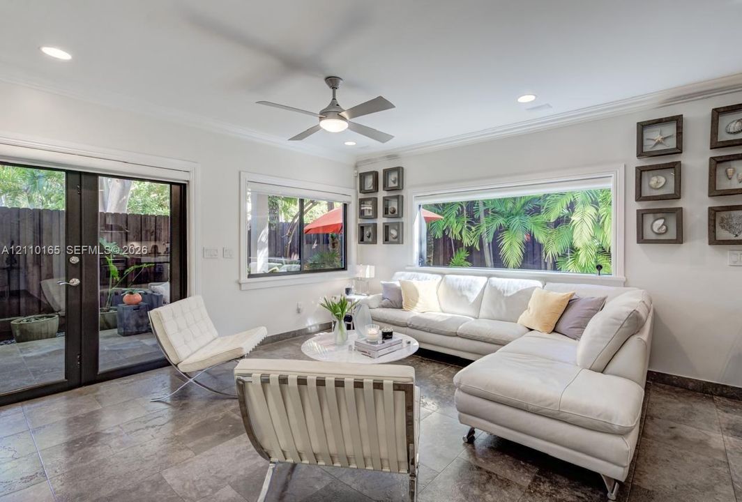 Living space featuring neutral stone-finish flooring, recessed lighting, a modern ceiling fan, crown molding, and large picture windows