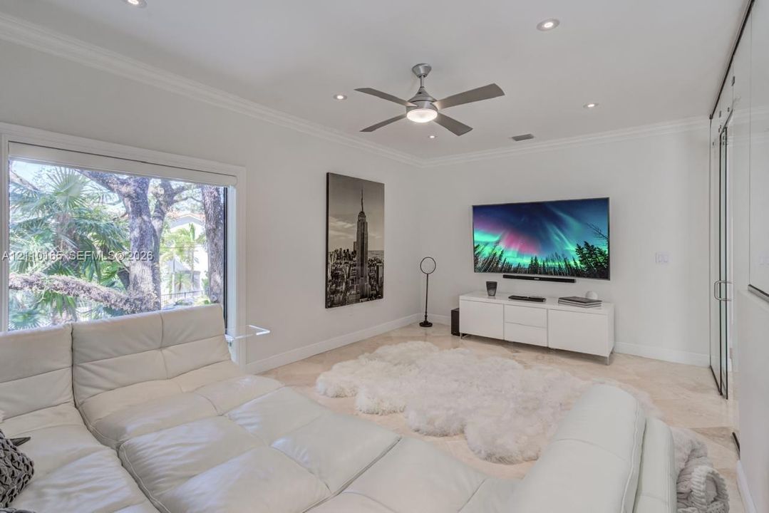Living area featuring stone tile flooring, recessed ceiling lighting, a contemporary ceiling fan, crown molding, and a wall of built-in cabinetry with mirrored doors