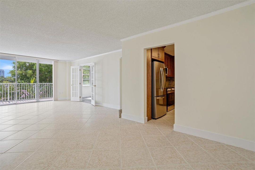 Spacious room featuring neutral tile flooring, floor-to-ceiling glass paneling, French doors, and stainless steel kitchen appliances