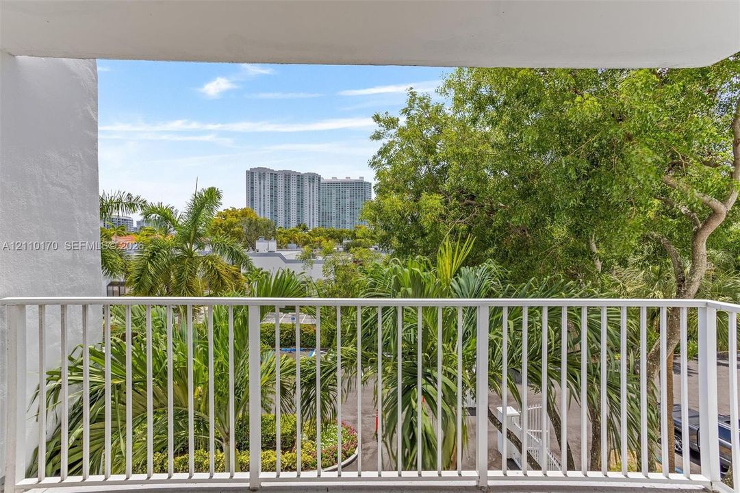 Private balcony featuring a white metal railing, mature palm trees, and exterior foliage