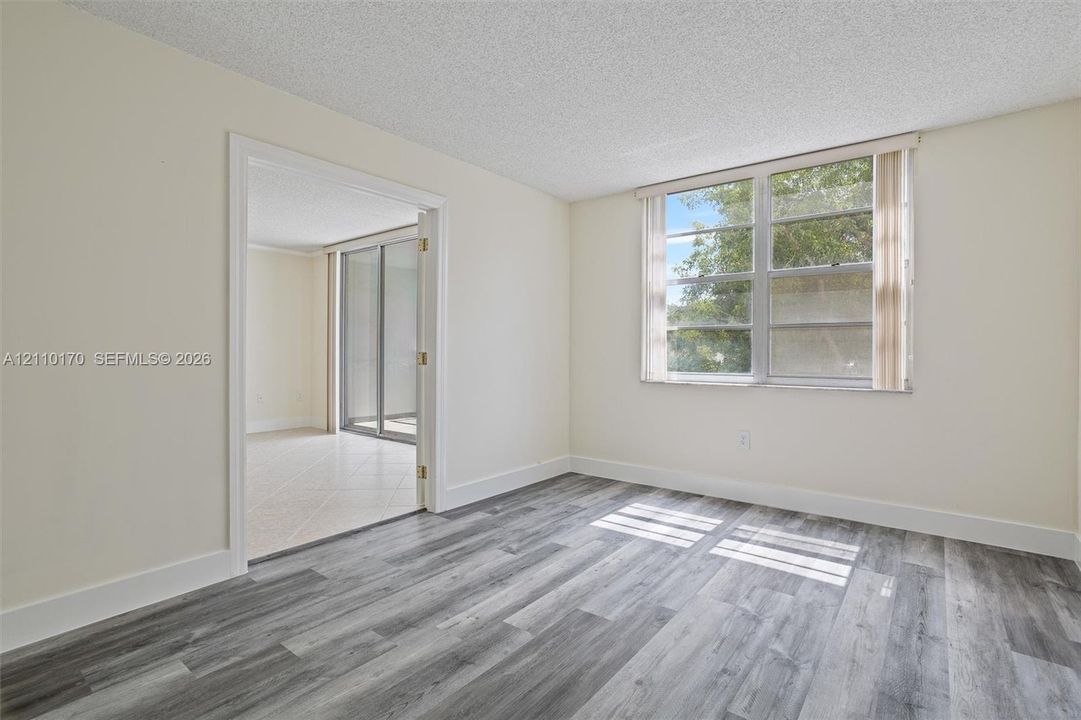 Interior space featuring wood-finish flooring, a multi-pane window with vertical blinds, and a wide doorway opening to a tiled area with sliding glass doors