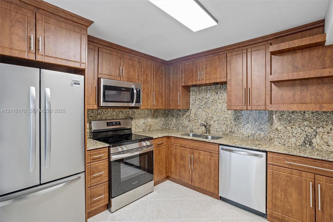 Kitchen featuring wood cabinetry, stone countertops, stone tile backsplash, stainless steel appliances, and built-in shelving