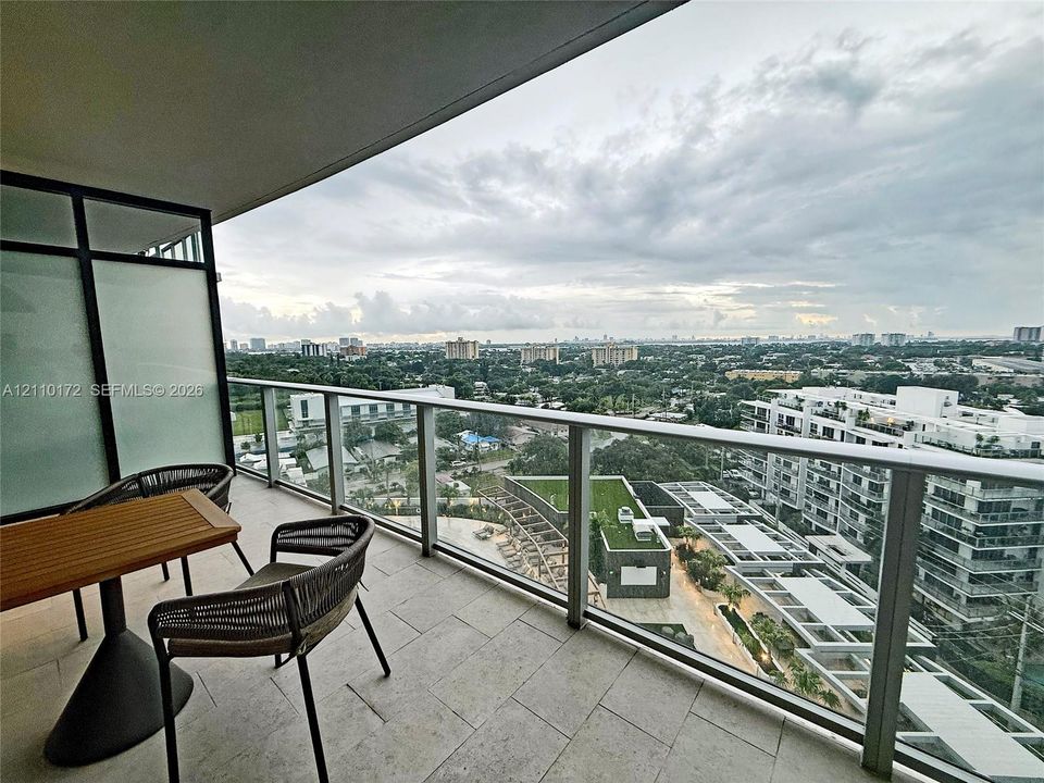 Covered balcony featuring stone flooring, a glass and metal railing system, and privacy glass panels