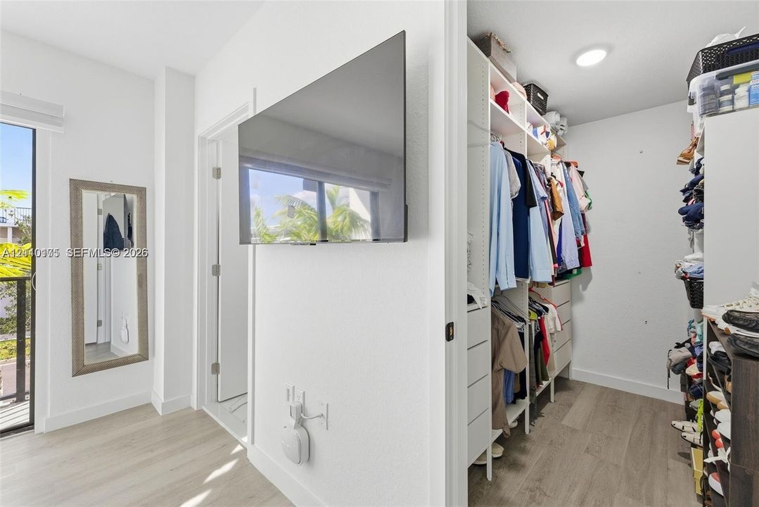 Walk-in closet featuring built-in shelving and drawer storage, wood-finish flooring, recessed lighting, and a glass-paned door