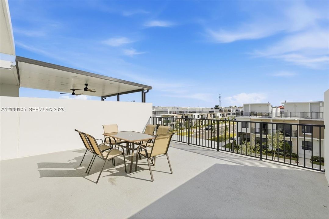 Expansive rooftop terrace featuring a covered patio area, ceiling fans, concrete flooring, and perimeter metal railings