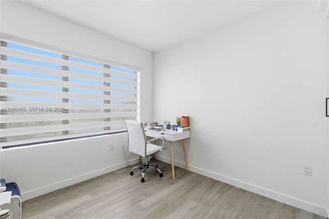 Interior room featuring wood-finish flooring, smooth white walls, and horizontal dual-layer light-filtering window shades