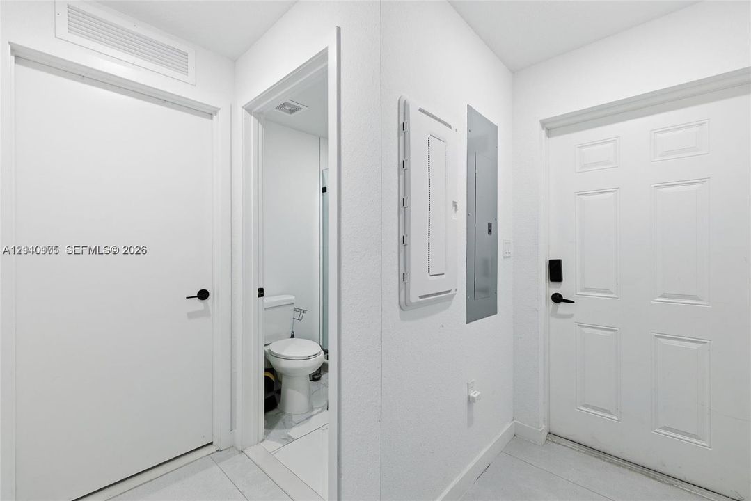 Interior hallway featuring paneled doors with matte black hardware, ceramic tile flooring, and integrated electrical service panel