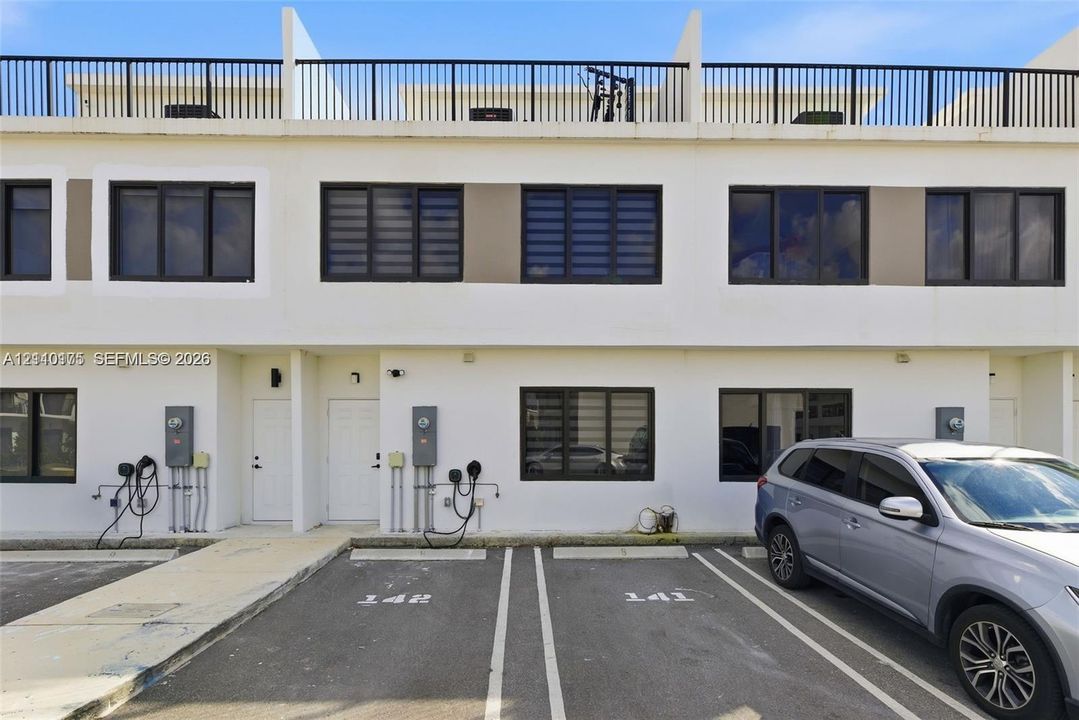 Contemporary two-story exterior with light-toned stucco facade, dark-framed windows, and private rooftop terrace featuring metal railing
