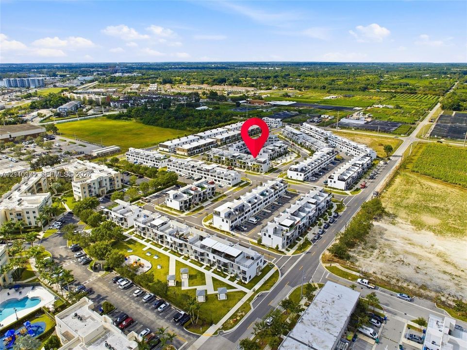 Aerial perspective of multi-level residential complex featuring paved surface parking, organized pedestrian walkways, landscaped common green spaces, and community swimming pool