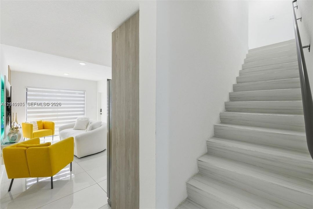 Staircase featuring wood-finish treads and a dark metal handrail, complemented by large-format tile flooring and a neutral color palette