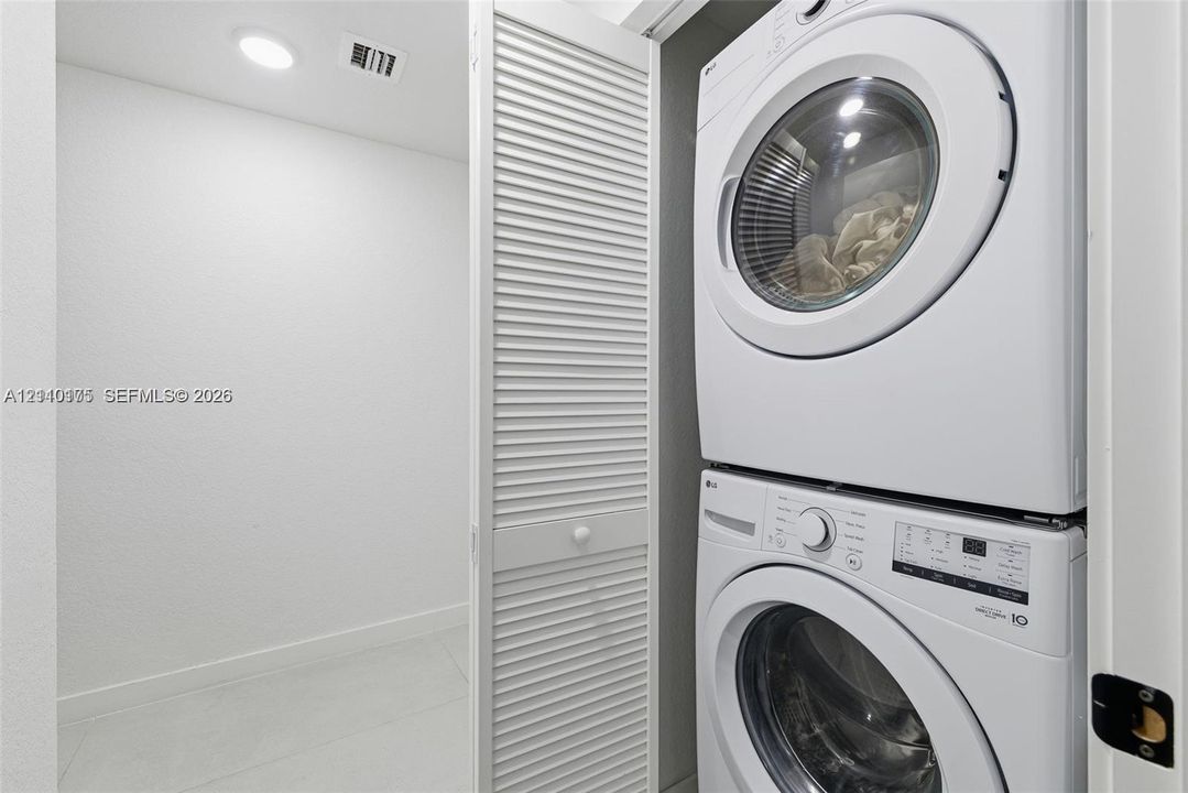 Laundry closet featuring stacked front-load appliances and louvered folding doors